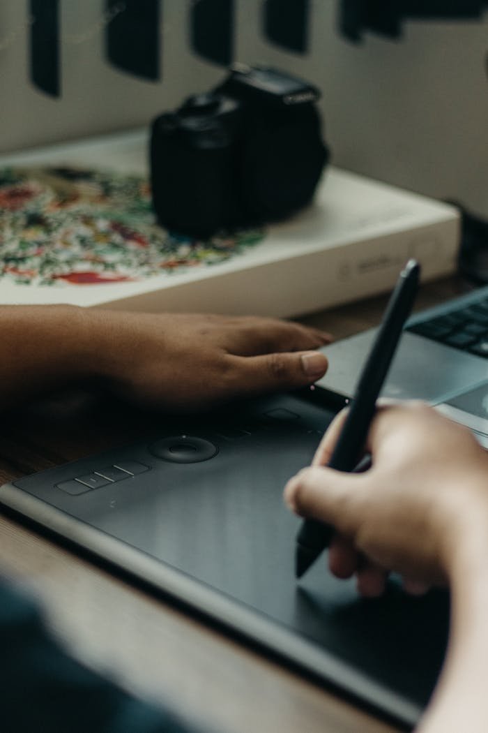 Hands using a stylus on a digital drawing tablet in a creative workspace.