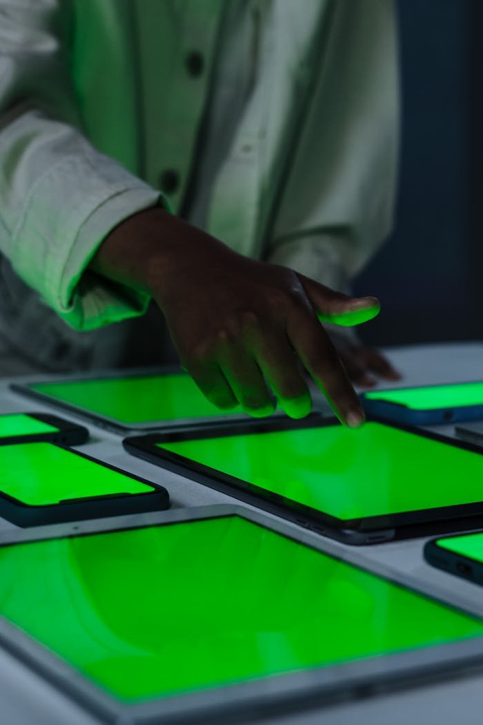 A person points at illuminated green tablets in a dark room, highlighting technology interaction.
